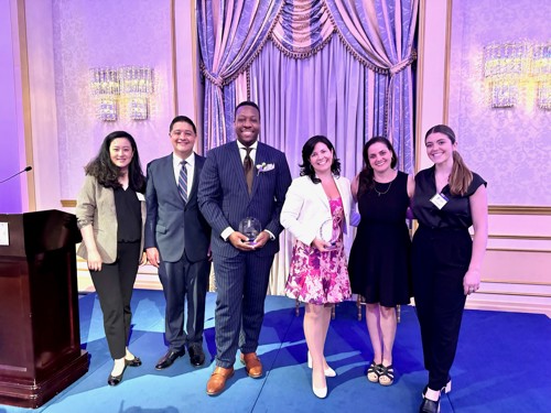 Nexus U. Sea holds his award and poses with 5 colleagues at the 2024 Partners of Justice Awards Gala