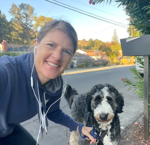 A colleague in workout clothes smiling while walking their brown, white, and black large dog in their neighborhood